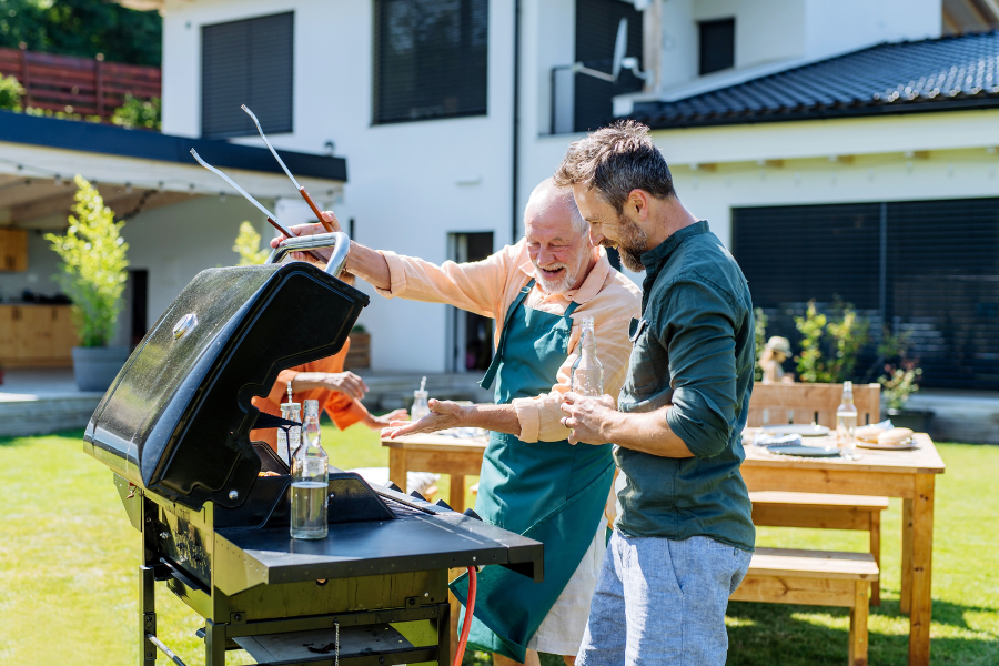 Moment complice père-fils autour d’un barbecue pour la Fête des Pères. Père et fils en train de préparer un barbecue ensemble dans le jardin.