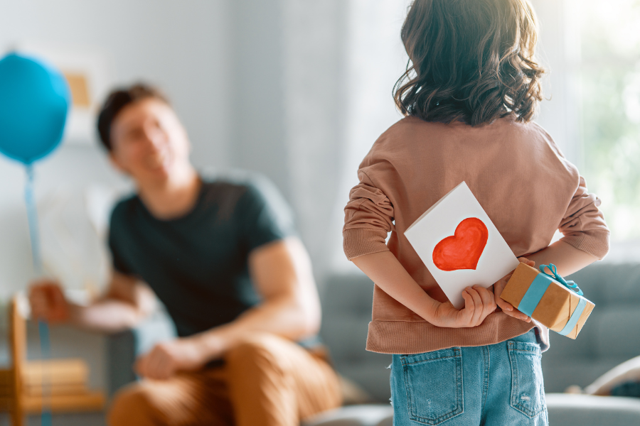 Un enfant cache une carte avec un cœur et un cadeau derrière son dos pour la fête des pères