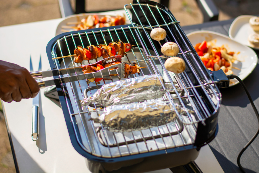 Barbecue électrique en pleine cuisson – profitez sans risque Barbecue électrique en fonctionnement avec brochettes et maïs en cuisson