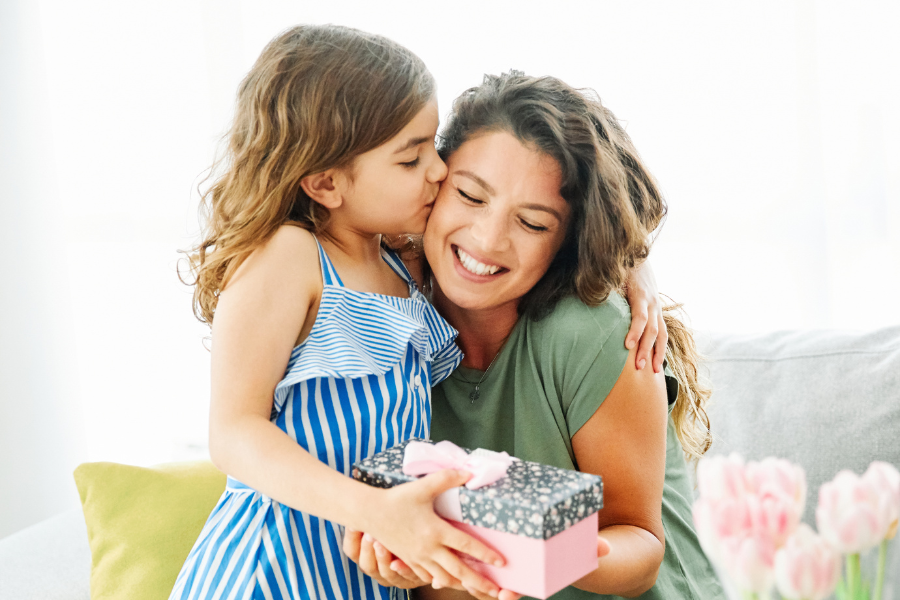 Enfant offrant un cadeau &agrave; sa m&egrave;re avec un bisou pour la f&ecirc;te des m&egrave;res dans un moment de tendresse
