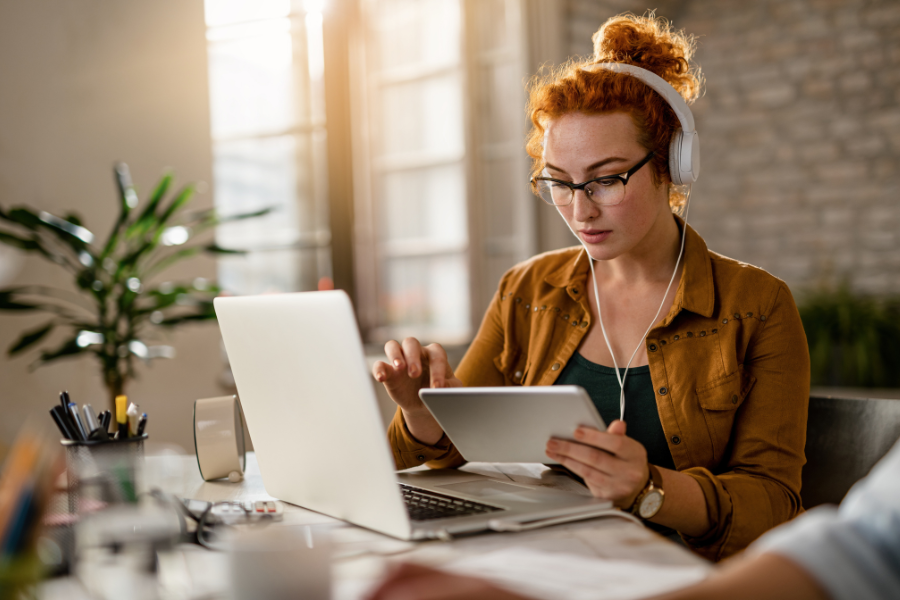 Jeune femme concentrée travaillant sur un ordinateur portable et une tablette avec un casque audio.