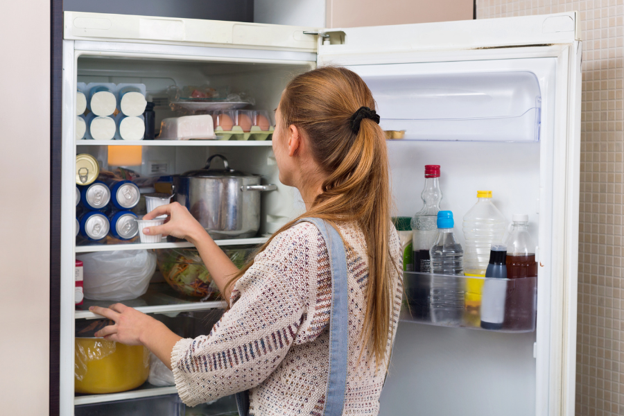 Comment bien organiser son réfrigérateur pour éviter la perte de froid – Conseils Gitem Femme rangeant son réfrigérateur ouvert rempli d’aliments et de boissons, illustration d’un frigo mal organisé pouvant entraîner une perte de froid