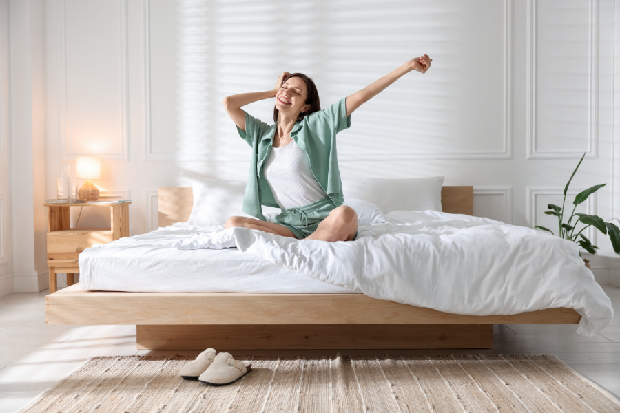 Femme souriante qui s&rsquo;&eacute;tire dans son lit apr&egrave;s une bonne nuit de sommeil gr&acirc;ce &agrave; une literie confortable