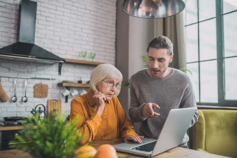 Une personne âgée apprend à utiliser un ordinateur portable avec l’aide d’un proche.